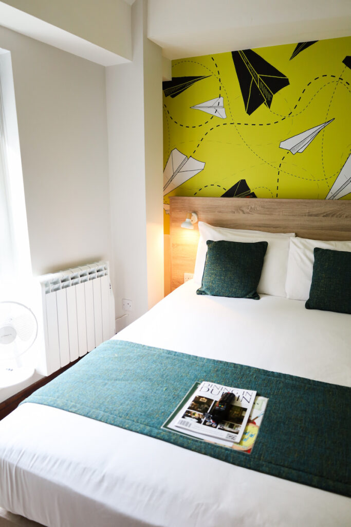 Stylish hotel room with bright paper plane mural, modern decor, cosy bed, and natural light. Perfect for a relaxing stay.