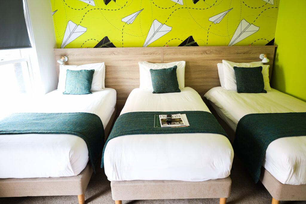 Cosy hotel room with three single beds, vibrant décor, plush pillows, and natural light. Perfect for a family stay.
