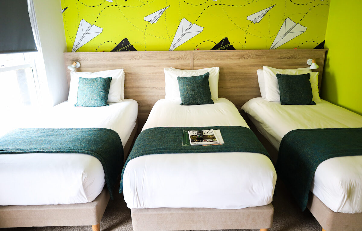 Cosy hotel room with three single beds, vibrant d&eacute;cor, plush pillows, and natural light. Perfect for a family stay.