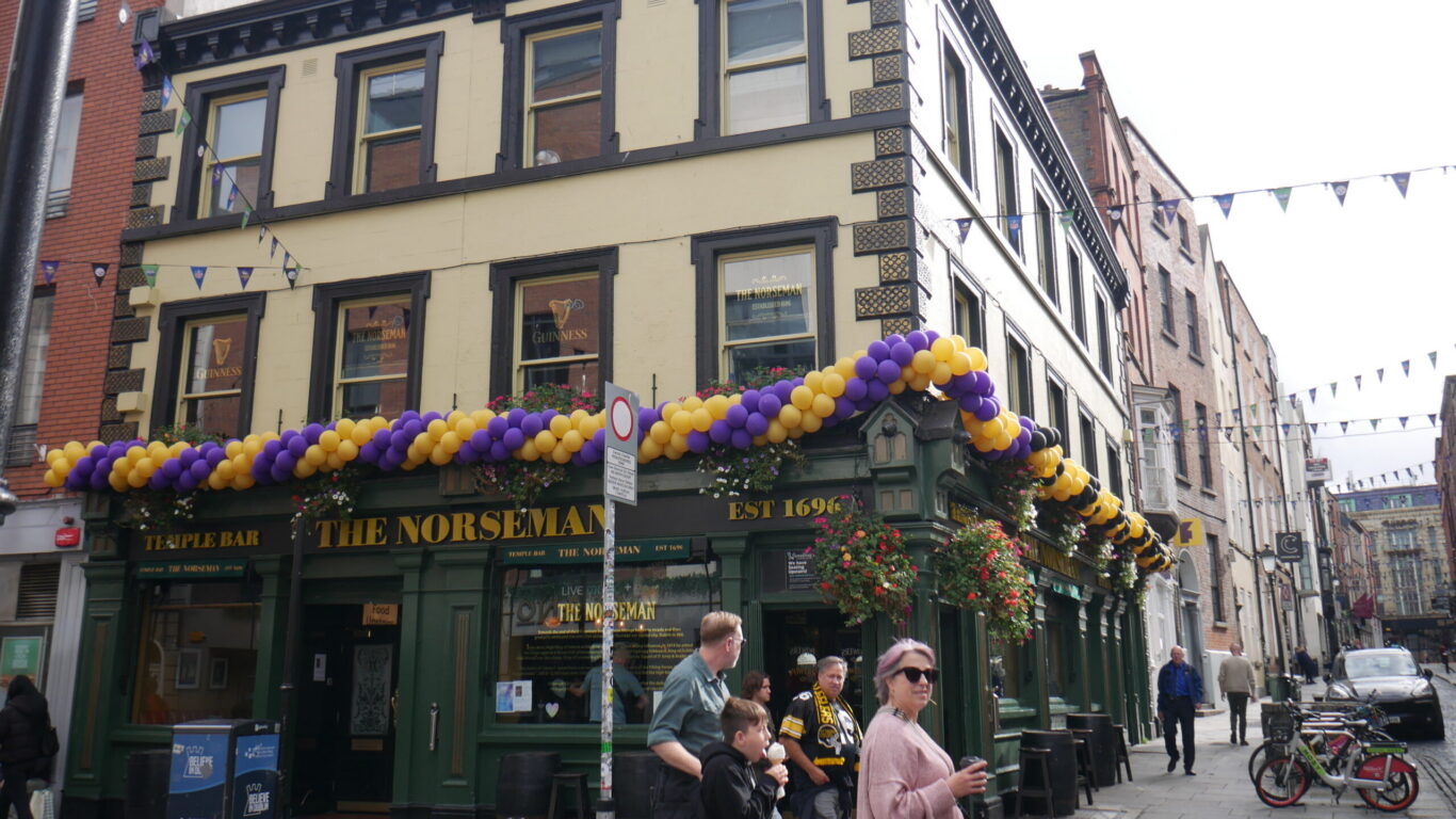 Historic pub with colourful balloons adorning the fa&ccedil;ade, vibrant city street scene, welcoming atmosphere near hotel.