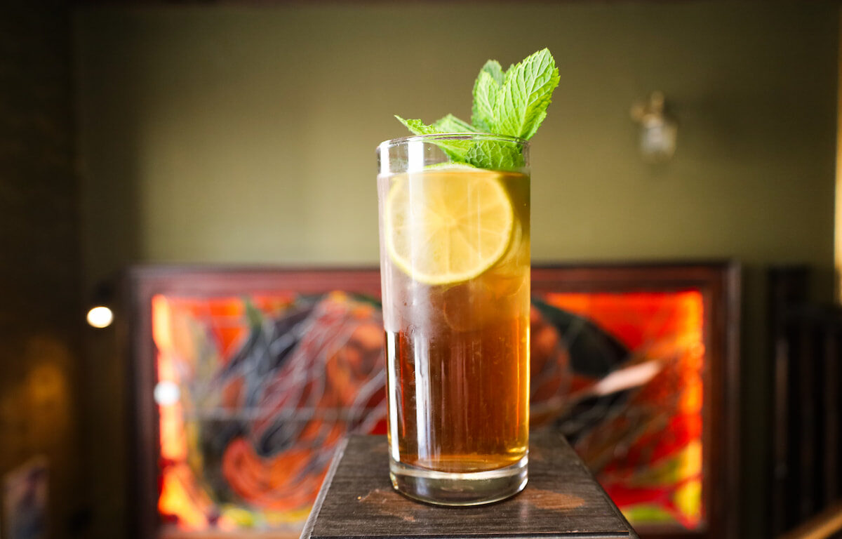 Refreshing cocktail with lemon slice and mint against vibrant art in a stylish hotel bar.