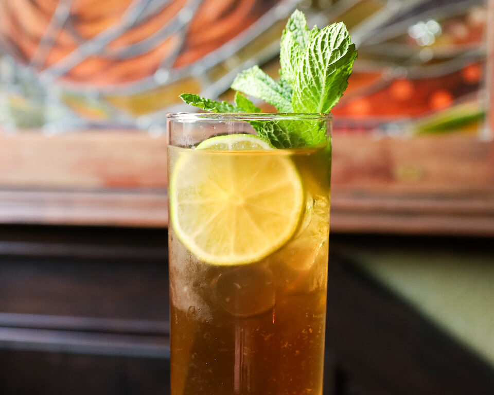Refreshing cocktail with lime slice and mint at elegant hotel bar with stained glass backdrop.