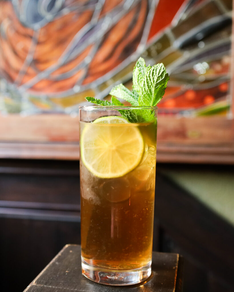 Refreshing cocktail with lime slice and mint at elegant hotel bar with stained glass backdrop.