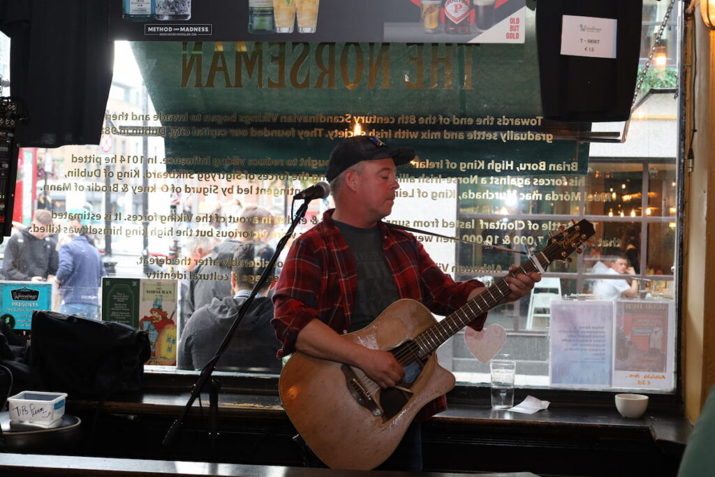 Live Music at Irish Pub Man playing guitar in lively pub with rustic decor, offering an authentic Irish music experience for hotel guests.