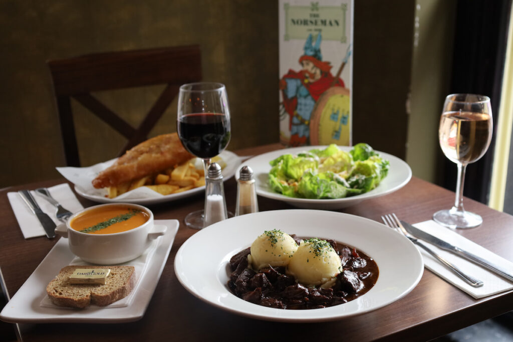 Guests enjoy a sumptuous hotel dining experience with fish and chips, soup, fresh salad, and wine in an elegant setting.